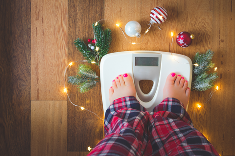Person wearing jammies checking their holiday weight on a scale with Christmas decorations surrounding them
